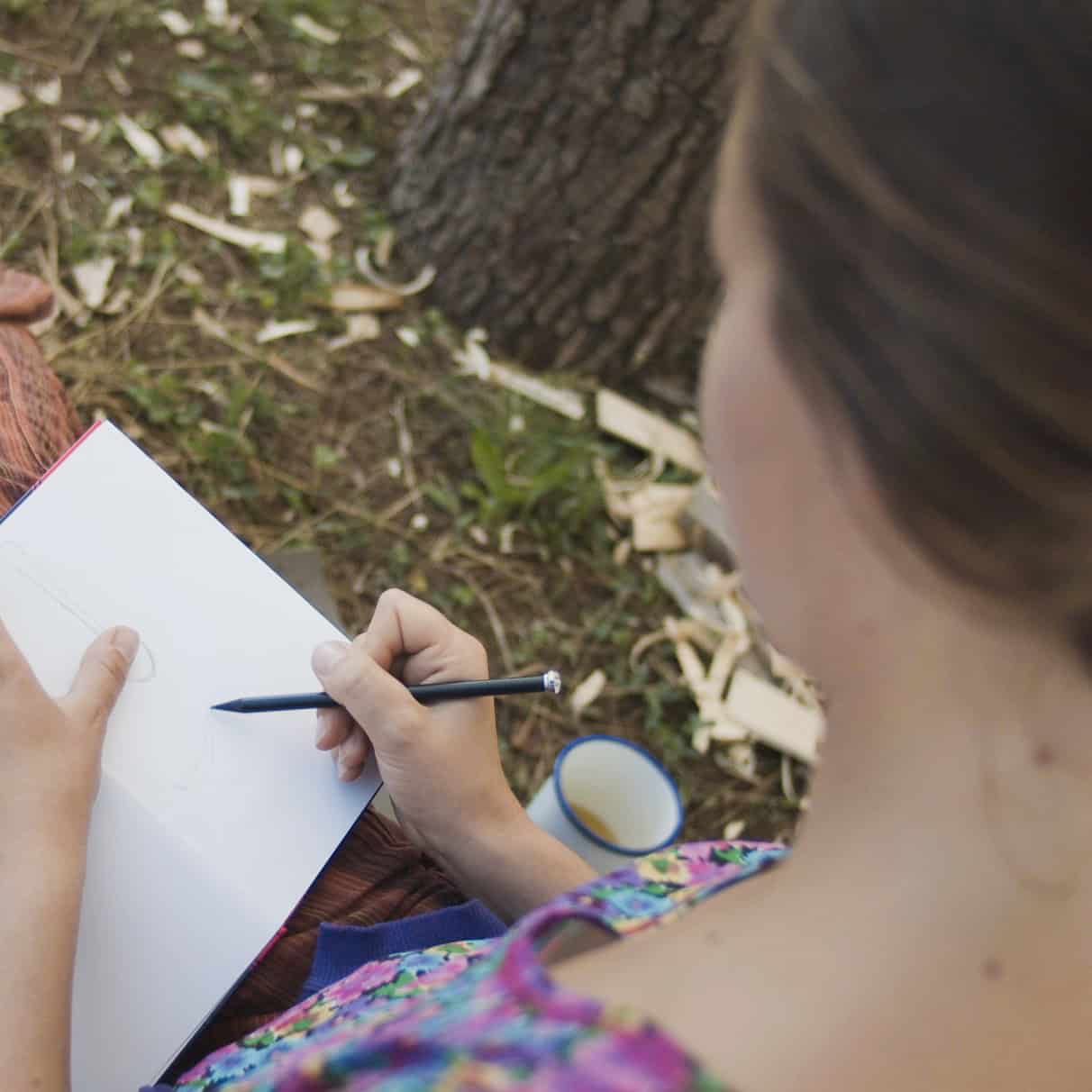 Porträt eines Kindes von hinten, das mit Stift auf Papier schreibt, mit Lupe und Natur im Hintergrund