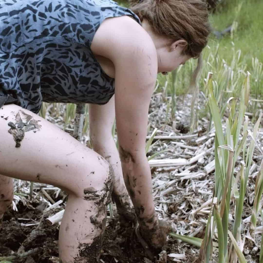 Porträt eines Kindes, das sich über einen Baumstamm beugt und Schlamm berührt