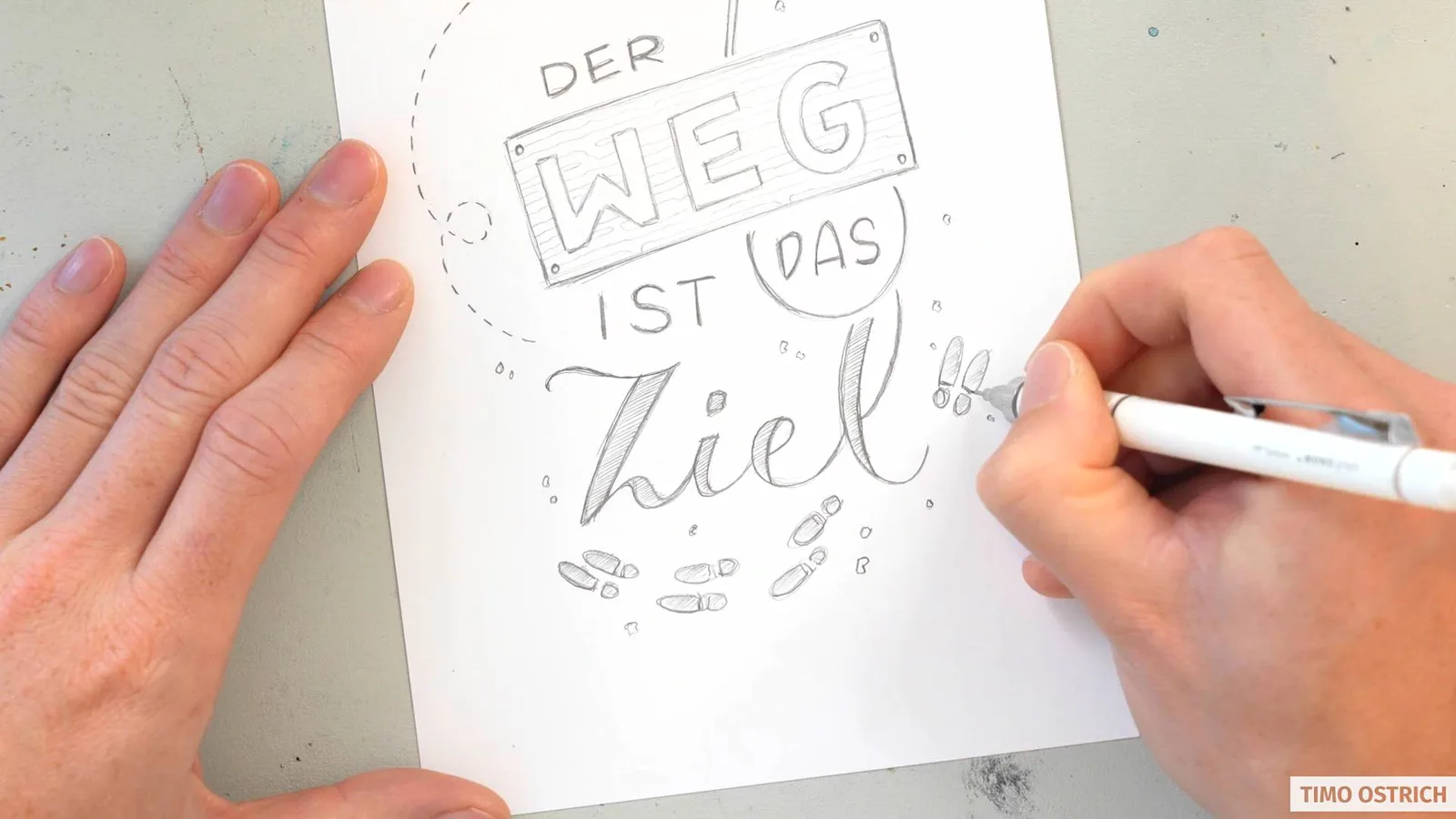 Hände zeichnen Text 'Der Weg ist das Ziel' mit Papierschiff-Illustration auf weißem Papier