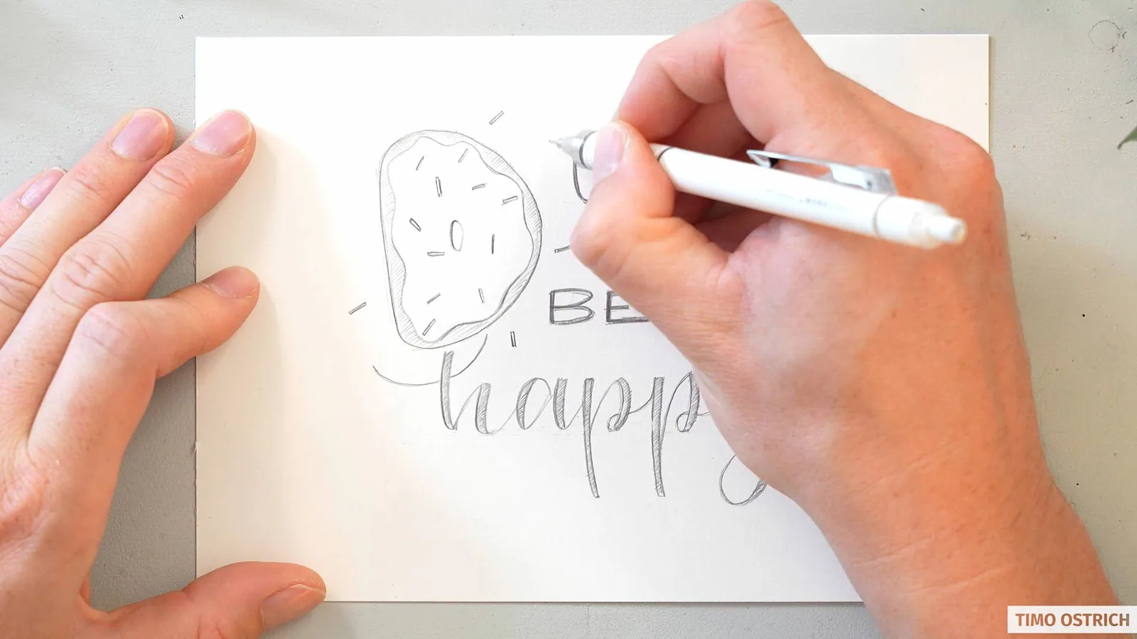 Hand zeichnet 'Donut worry be happy' mit Donut-Illustration auf weißem Papier