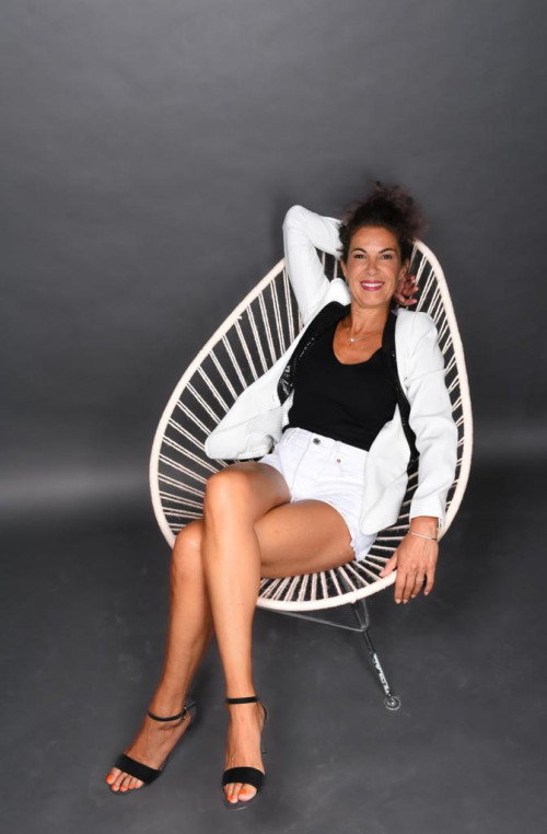 Portraitfoto von Jessica Mentrup auf weißem Stuhl in weißem Anzug vor grauem Hintergrund