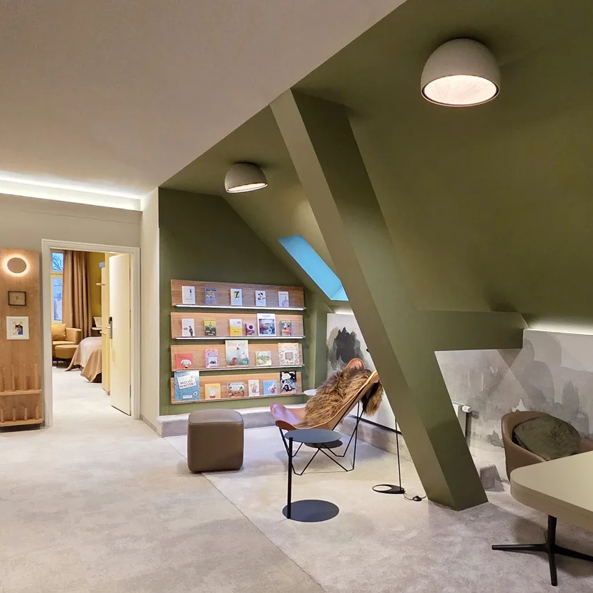 Hotelflur mit Dachschräge, Bücherregal und moderner Lichtplanung
