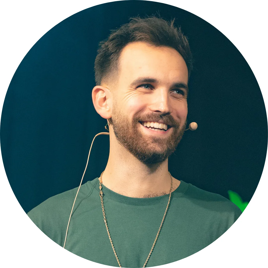 Porträt Maik Baum, Mann mit Headset, grünem Shirt und Kette auf dunklem Hintergrund