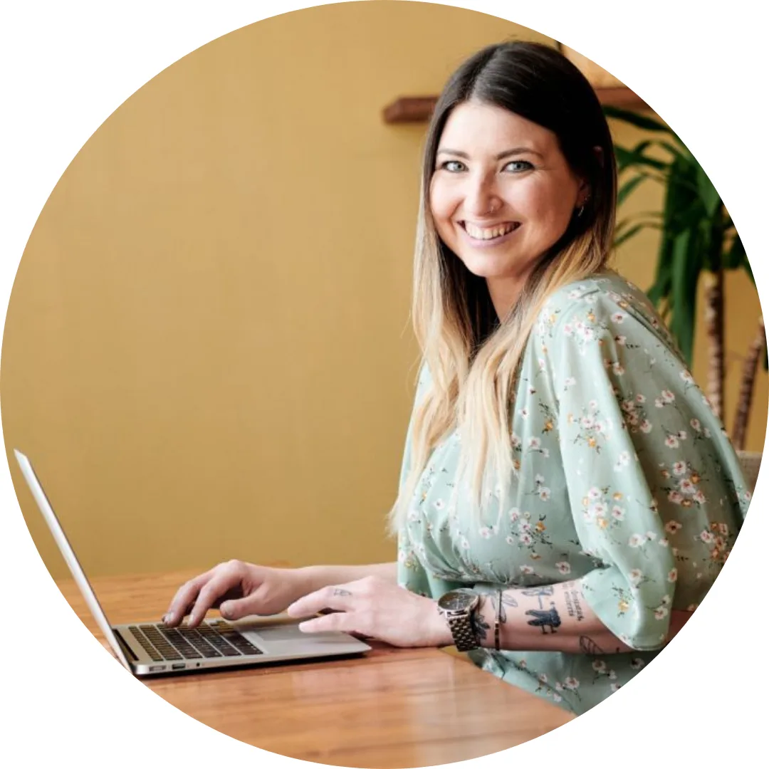 Katrin Steck Portrait – Frau mit braunem Haar in gemustertem Hemd am Laptop vor gelbem Hintergrund
