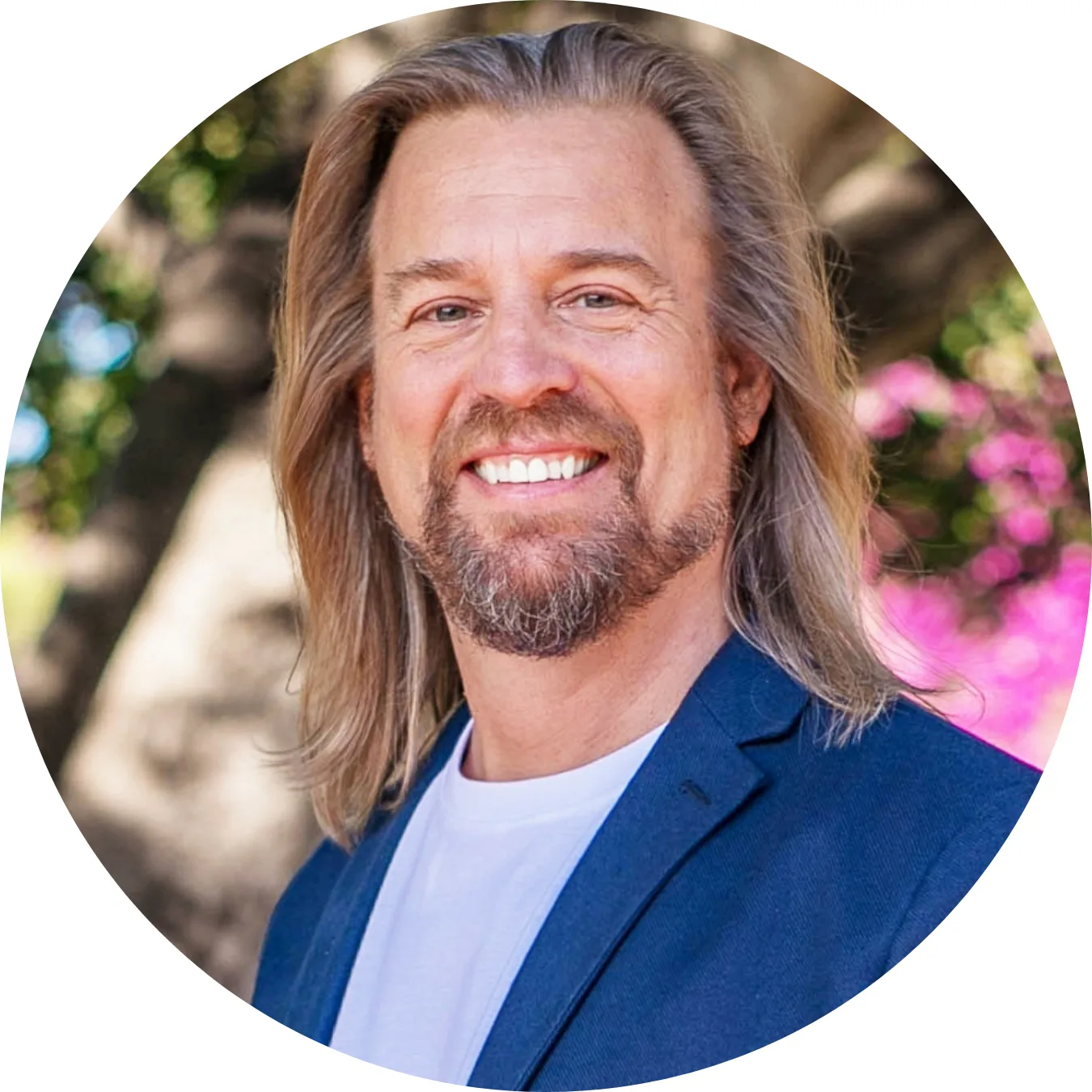 Dr. Marc Stollreiter, Mann mit langen braunen Haaren und Bart in blauem Blazer vor verschwommenem Hintergrund