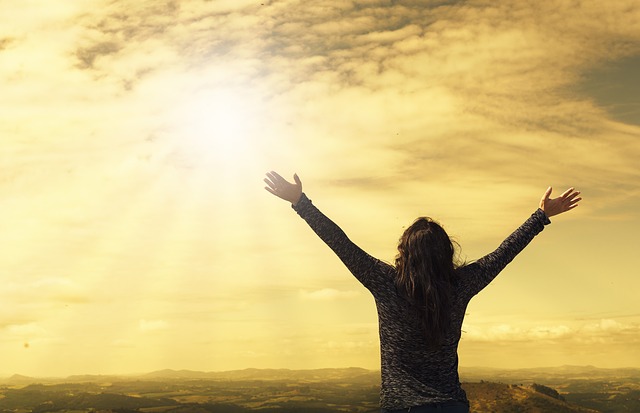 Frau mit ausgestreckten Armen vor goldenem Himmel, symbolisiert Freiheit und Loslassen