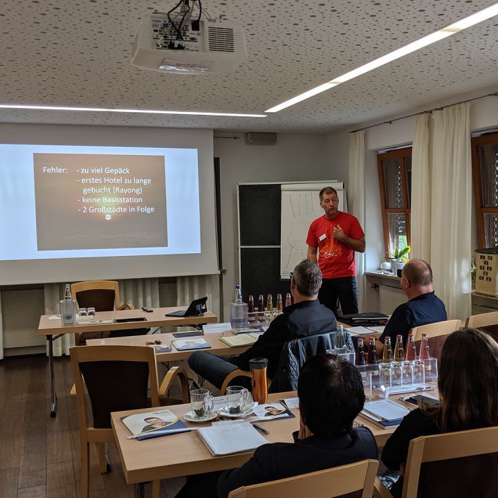 Tim Saladin präsentiert in rotem Shirt vor Publikum in Seminarraum mit Beamer-Präsentation
