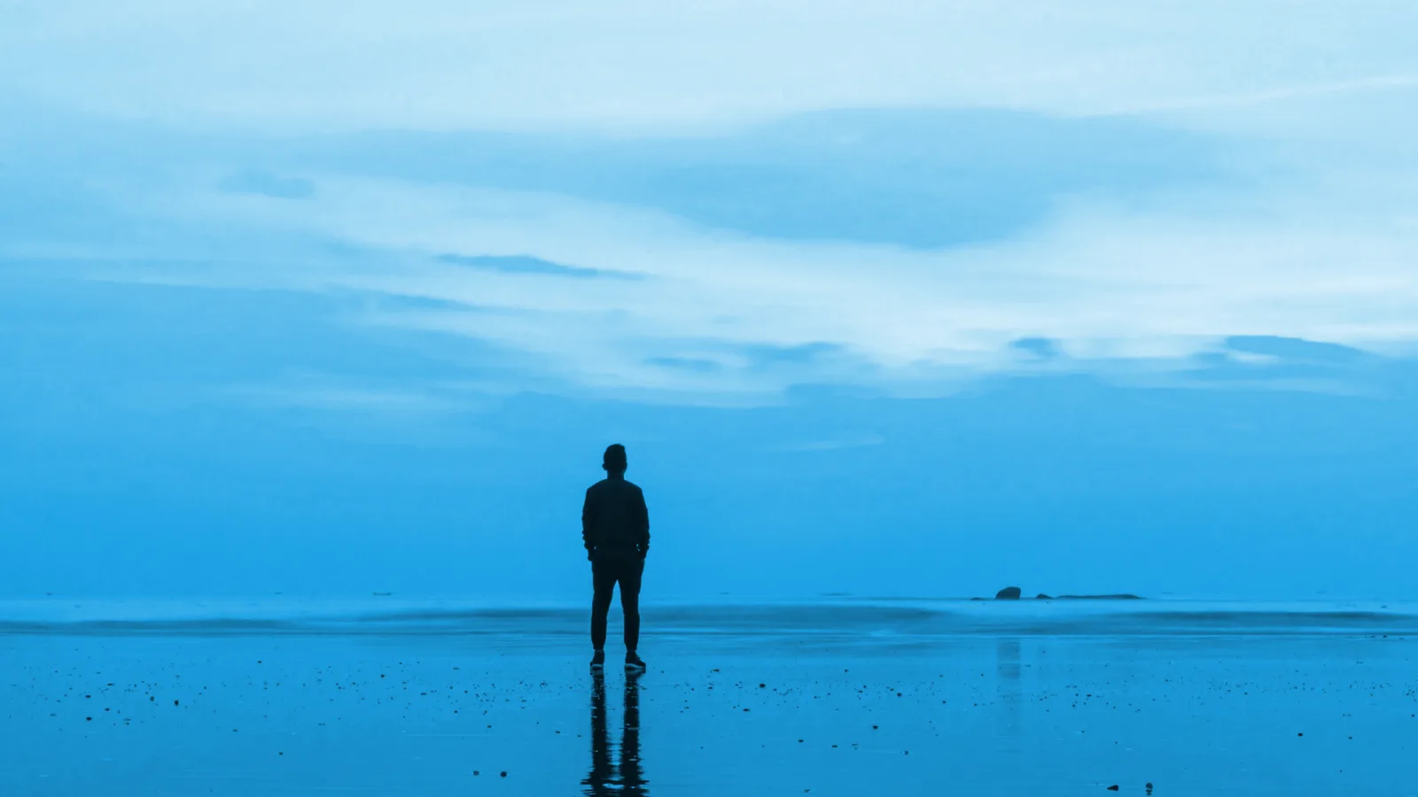 Live-Erfolgsseminar – Lösungen für ein selbstbestimmtes Lebe 2 Person steht allein am Strand mit Blick aufs Meer unter blauem Himmel