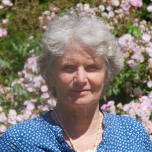 Porträt Dr. Deborah Collins MD – Frau mit silbernen Haaren vor Blütenhecke