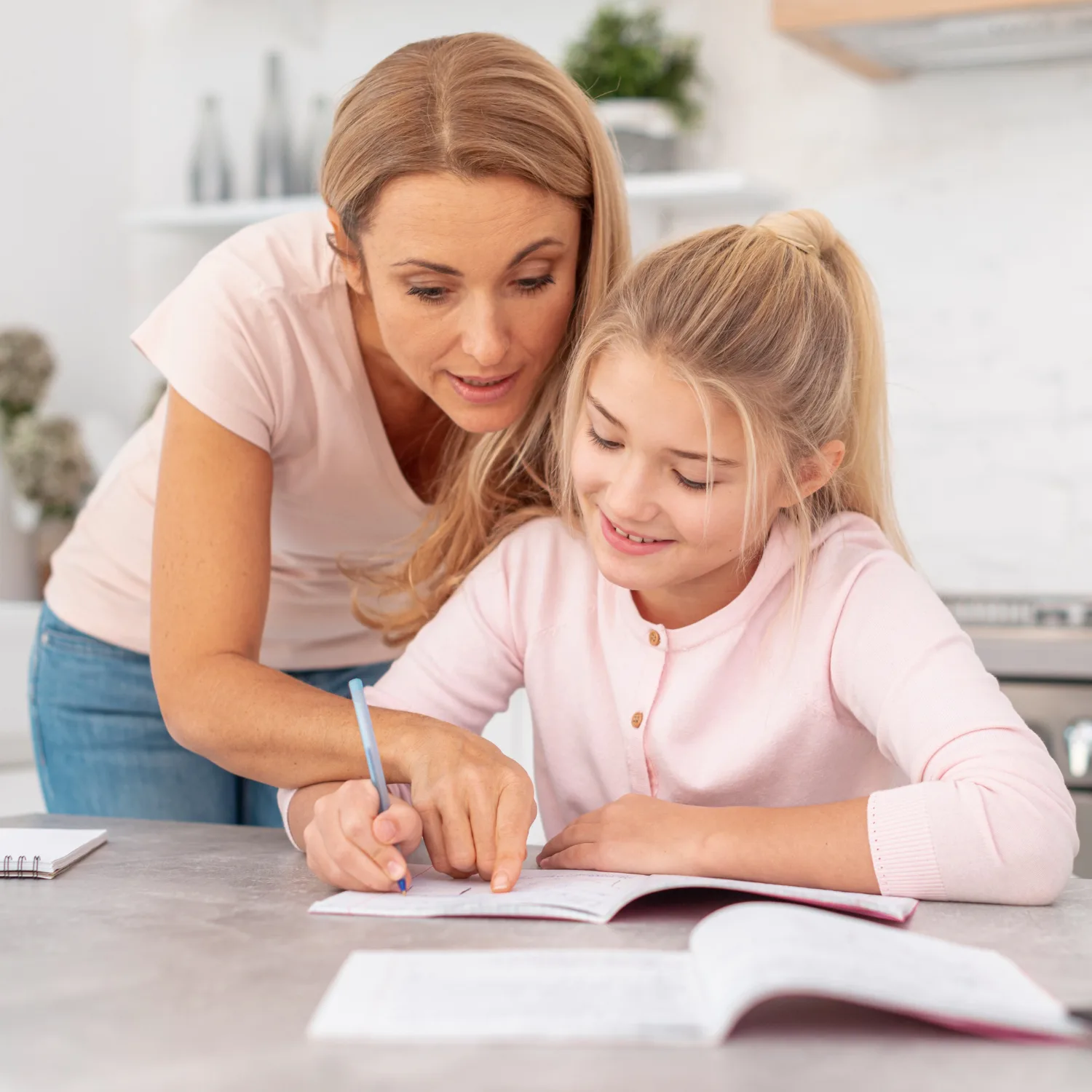 Mutter zeigt Tochter Schreibübungen in Arbeitsheft, moderne helle Küche