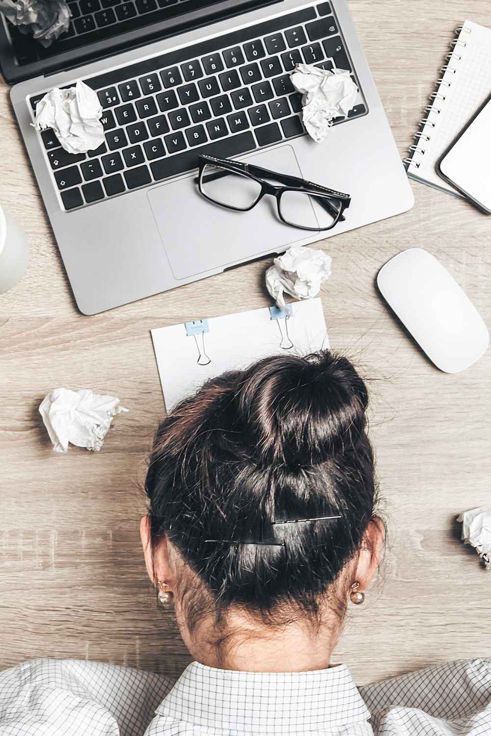 Draufsicht auf Laptop mit zerknitterten Papierbällen, Brille, Notizbuch und weibliche Person von oben