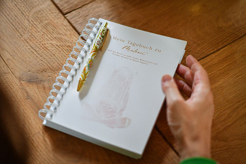 Hand hält aufgeschlagenes Maloori Spiraltagebuch mit Stift