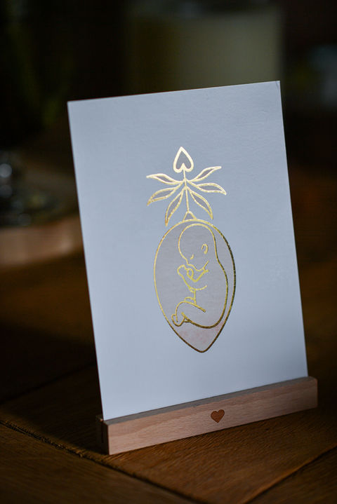 Grußkarte mit goldenem Herzdesign und Fetus-Illustration auf Holzständer