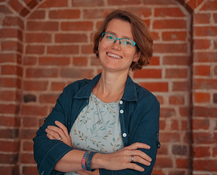 Nicole Wenzel mit Brille und Jeansjacke vor roten Ziegeln