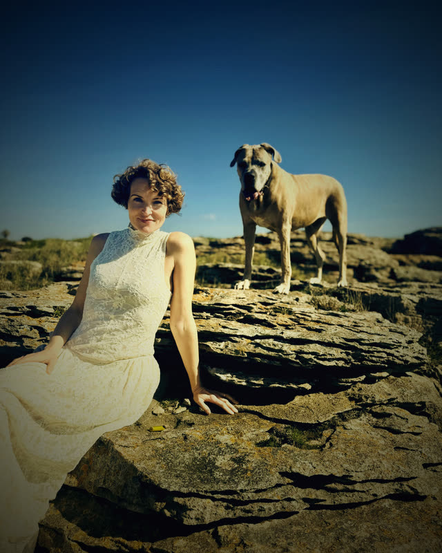 Stefanie Bruns in weißem ärmellosen Kleid mit großem weißem Hund im Freien bei blauem Himmel