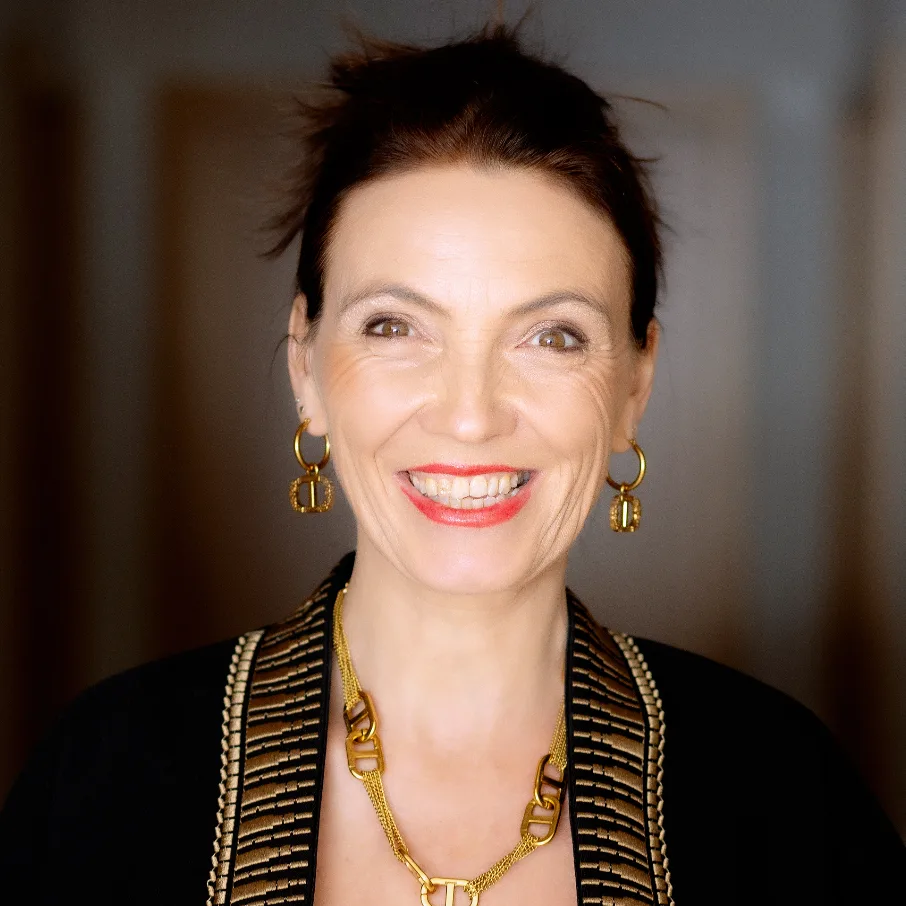 Carmen Duffner Profilbild mit Dutt, goldener Kette und Ohrringen vor neutralem Hintergrund