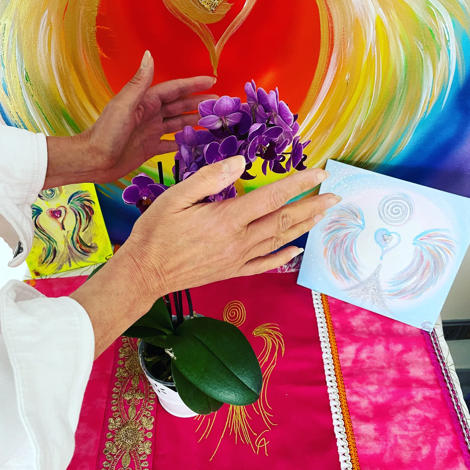 Carmen Duffner hält lila Orchidee vor Regenbogen-Energiebild und Zeichnungen