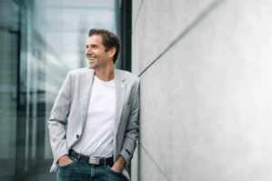 Mann in grauem Blazer und weißem Shirt an moderner Bürogebäude-Fassade