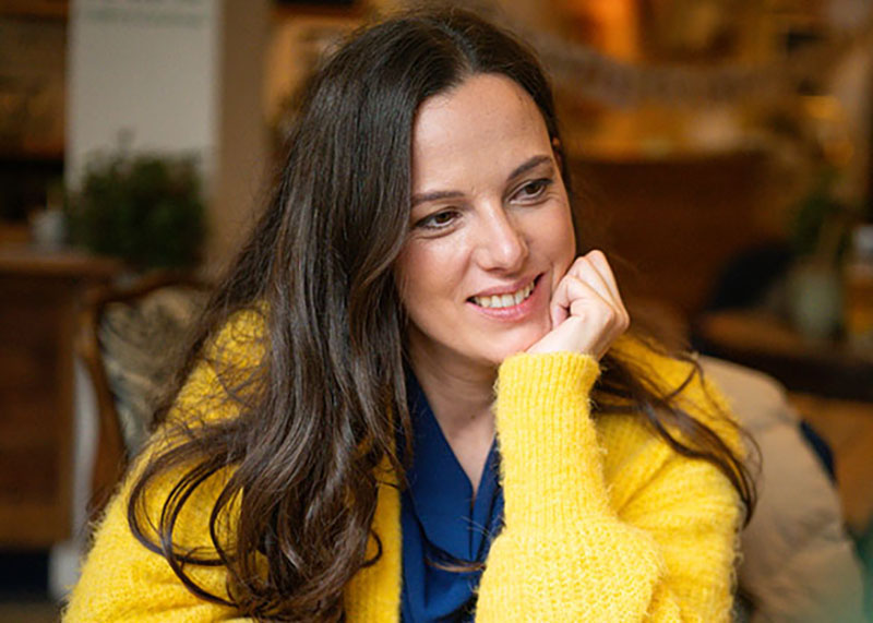 Dr. Martina Wengenroth lächelnd in gelbem Cardigan und dunklem Top vor unscharfem Interior