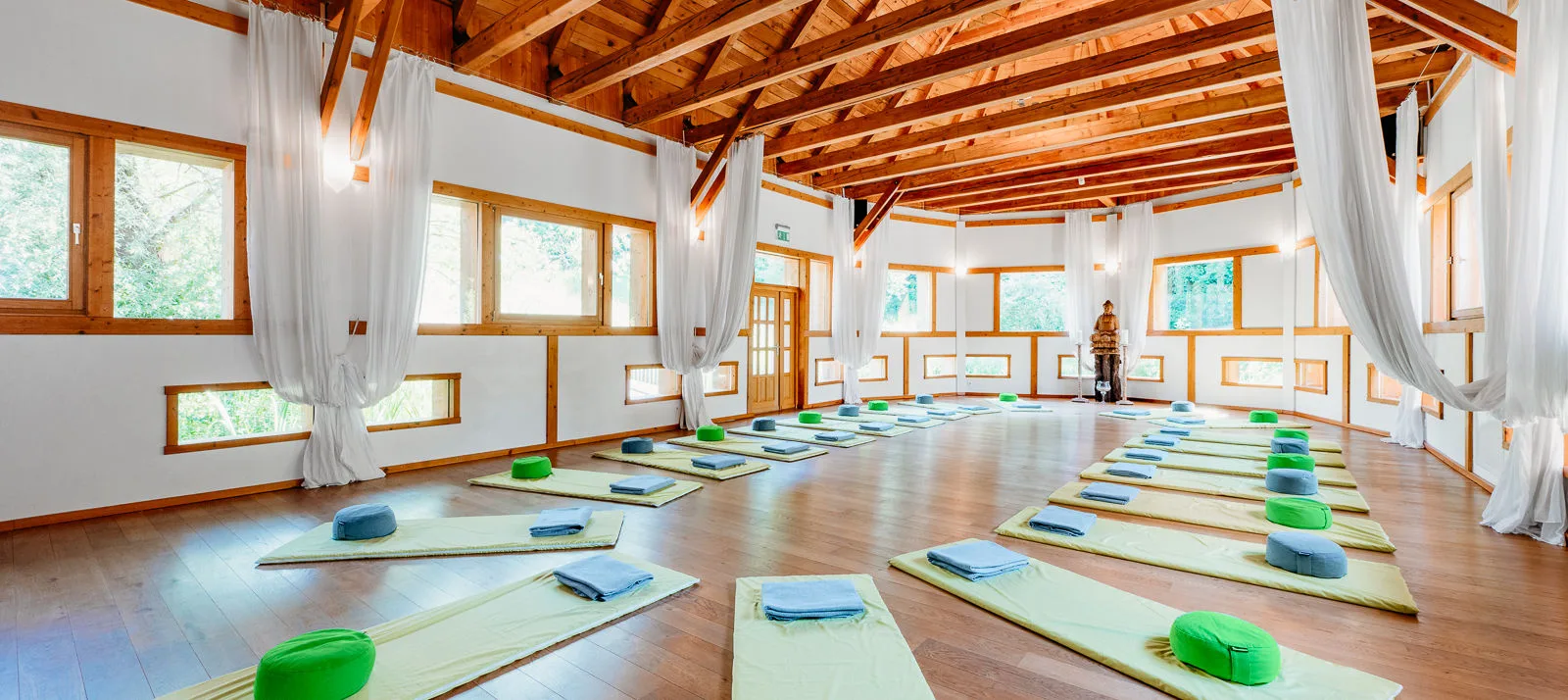 Yoga-Seminarraum mit Holzdecke, Yoga-Matten und Meditationskissen, große Fenster