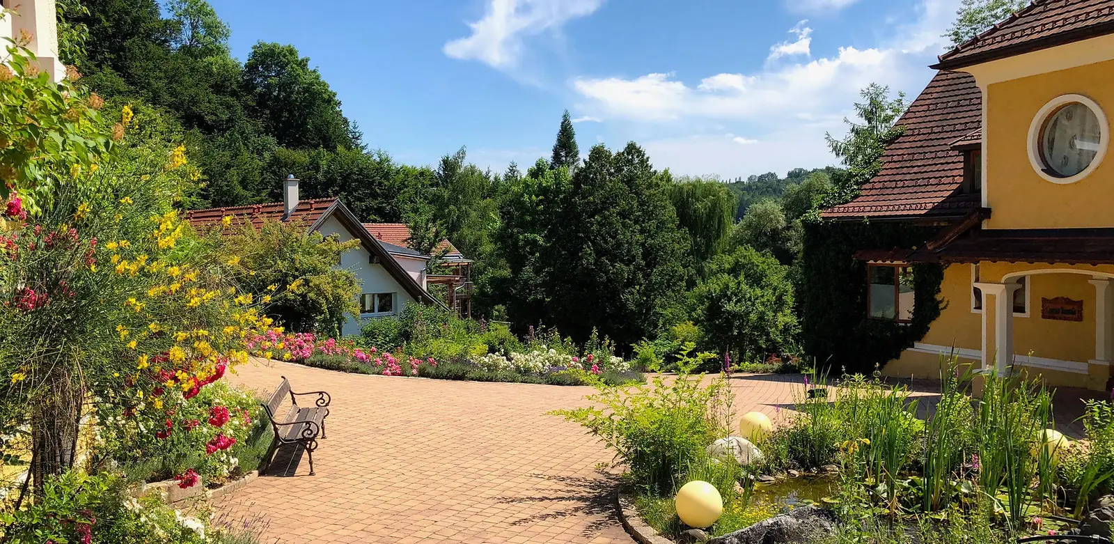 Ausbildungsstätte TamanGa mit gelben und weißen Häusern, Garten mit Blumen, Parkweg