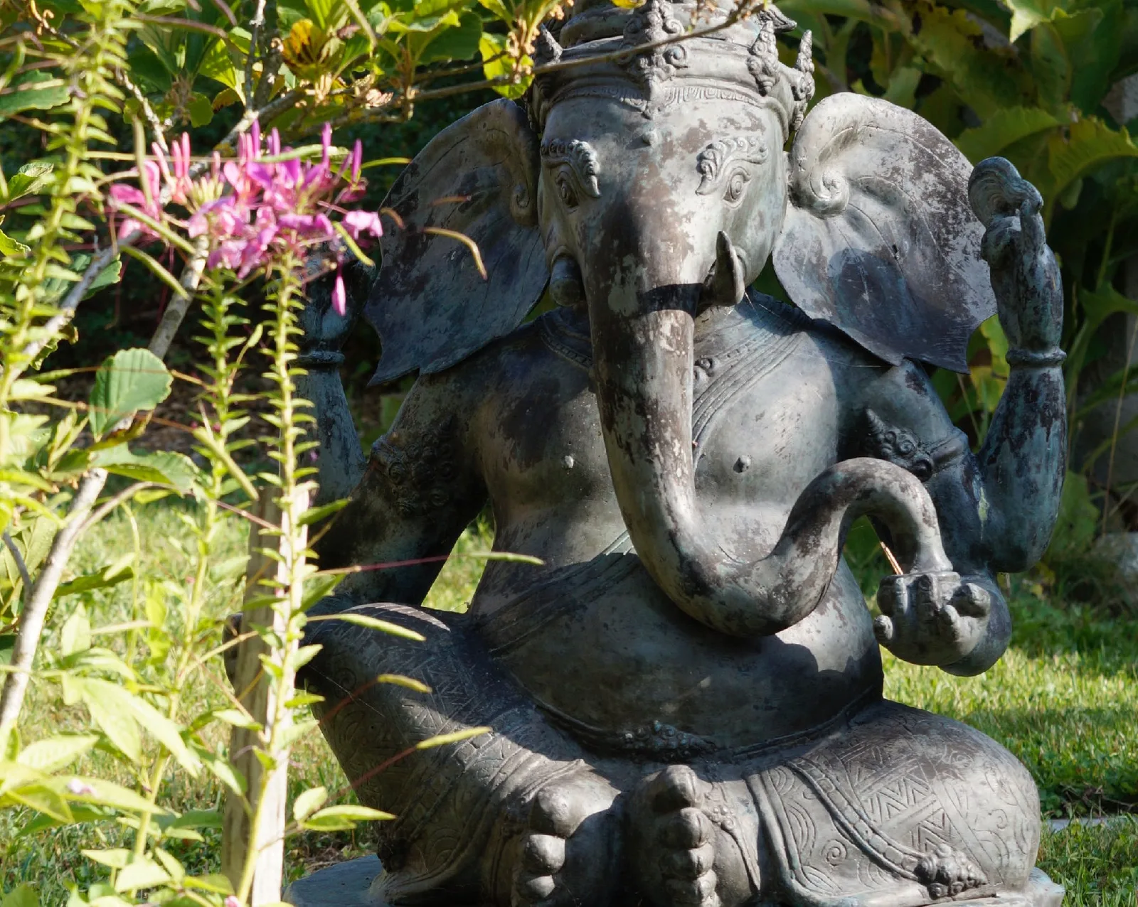 Ganesha-Statue aus Stein im grünen Garten umgeben von Blüten und Grün