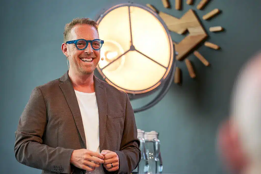 Norman Gräter lächelnd vor beleuchteter Uhr im Business-Setting