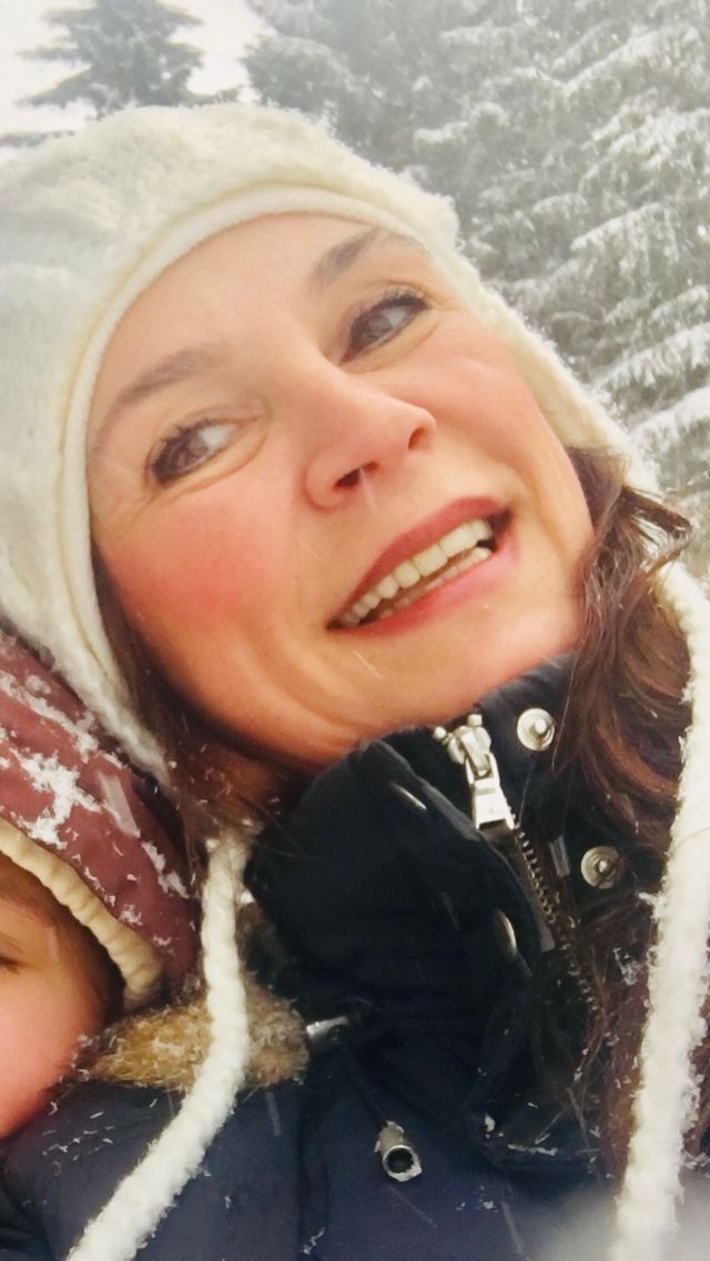 Frau im Schnee mit weißer Mütze und dunkler Jacke, lächelnd