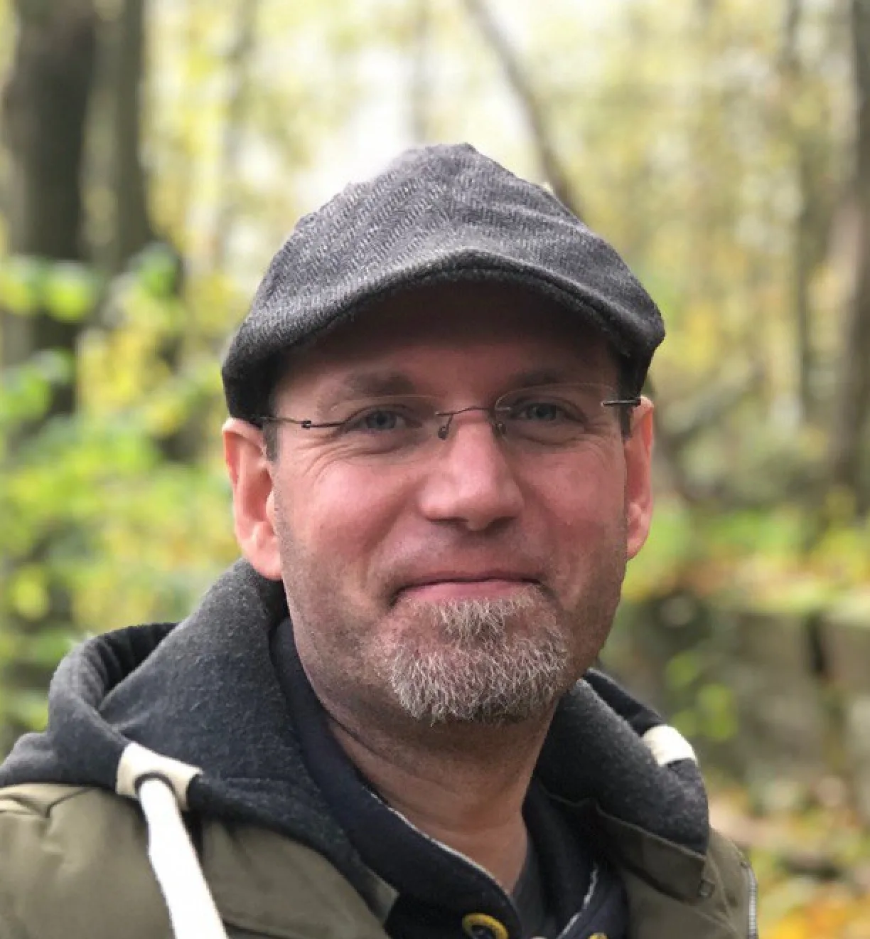 Mann mit Brille und grauer Mütze vor grünem Hintergrund