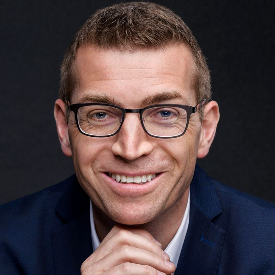 Michael Pauli Porträt mit Brille vor dunklem Hintergrund, trägt dunkles Hemd, lächelt zur Kamera