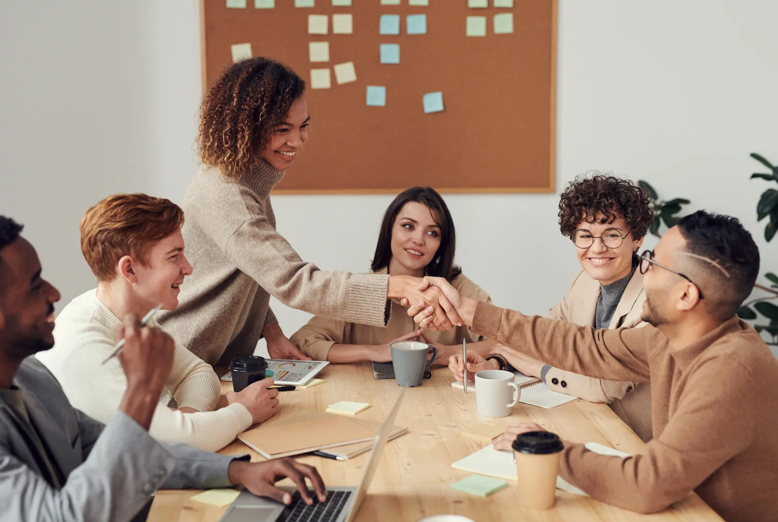 Foto Business-Meeting mit Teamarbeit: Mehrere Personen am Tisch, alle happy und konzentriert, mit Getränken und Unterlagen