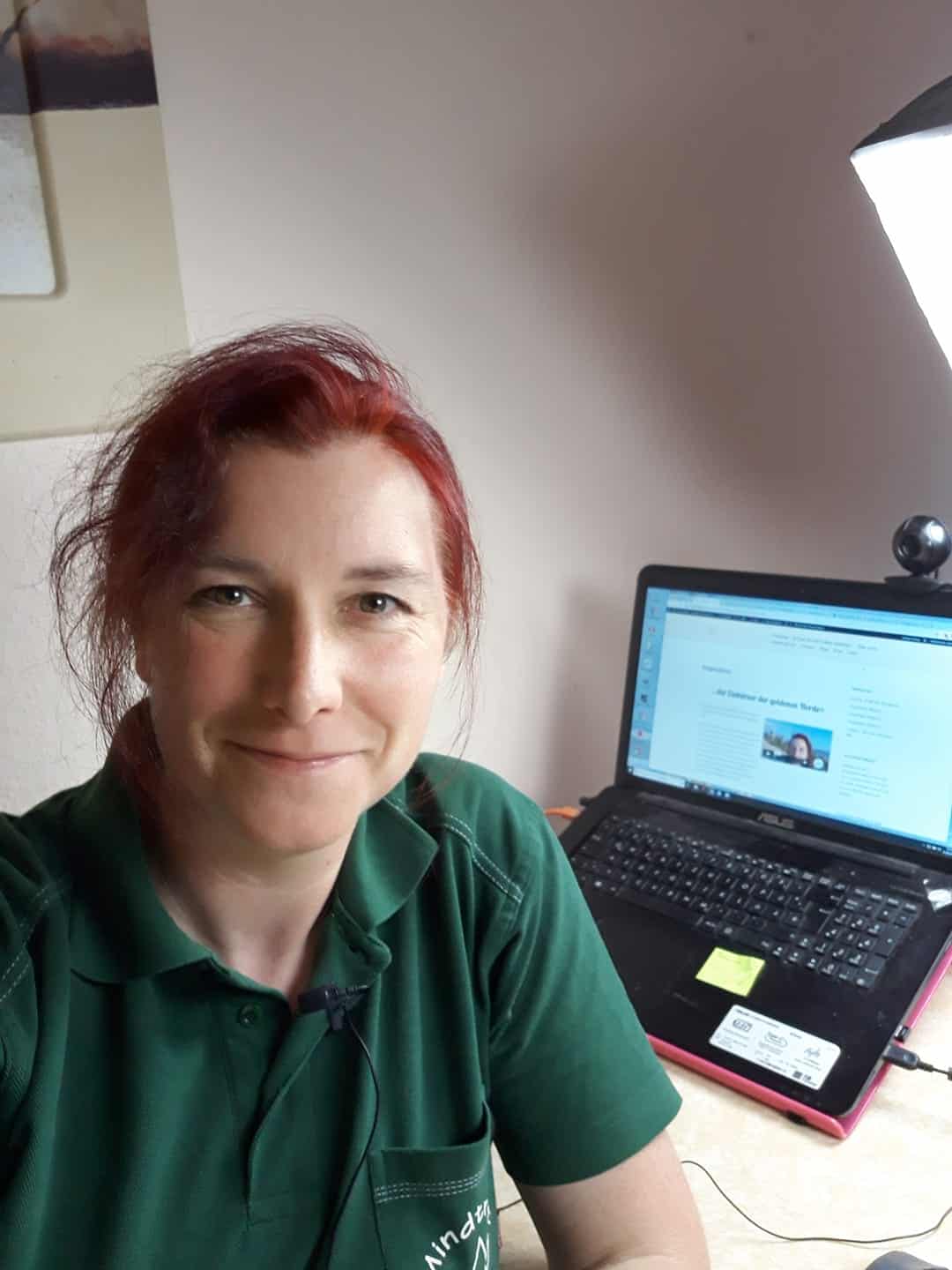 Nicole Hehnke mit roten Haaren in grünem Polo-Shirt vor Laptop, lächelnd