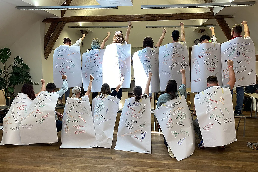 Gruppe hält Flipchart-Blätter mit handschriftlichen Notizen und Armen nach oben