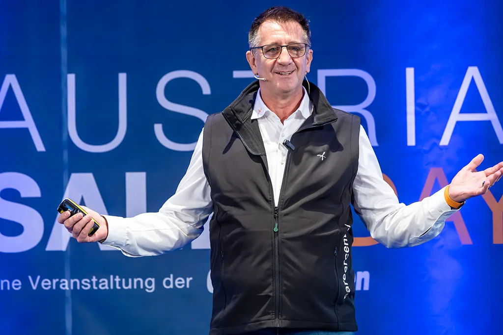 Günther Mathé spricht vor blauem Hintergrund bei Präsentation auf Bühne