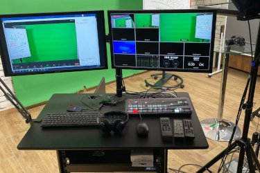 Videostudio-Arbeitsplatz mit Mischpult, Monitor und grünem Hintergrund
