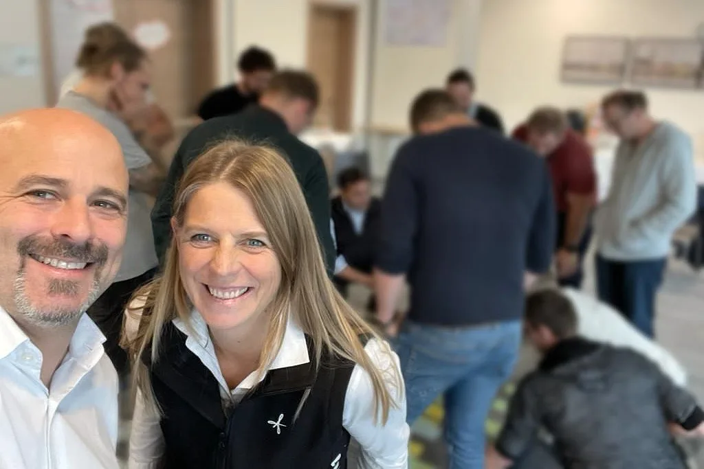 Zwei Personen lächeln in die Kamera bei Veranstaltung mit Publikum im Hintergrund