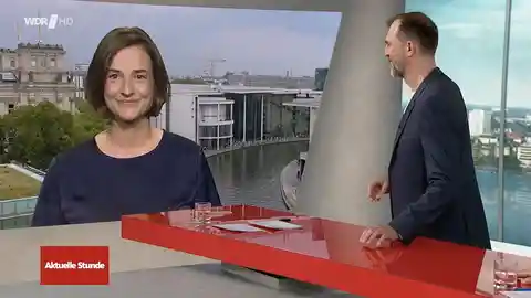 Videostandbild: Frau im Interview auf Nachrichtenset mit Skyline im Hintergrund