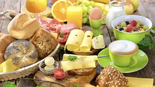 Frühstückstisch mit Brot, Käse, Orangensaft, Müsli und Tee in grüner Tasse
