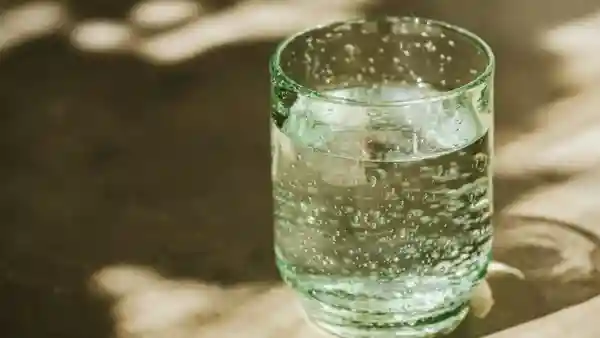 Glas mit Wasser und Eiswürfeln auf sonniger Oberfläche