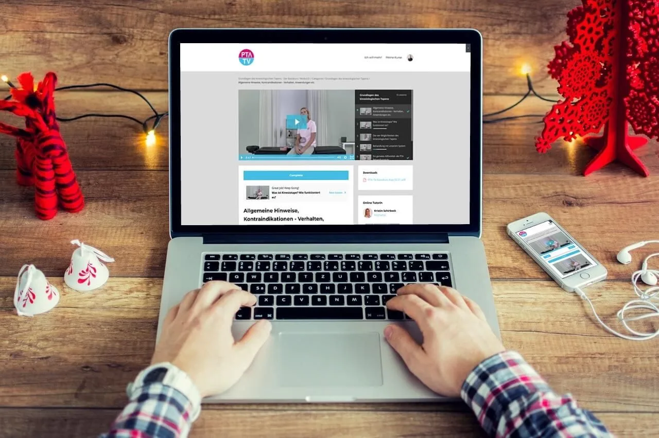 Laptop-Bildschirm zeigt PTA TV Kursseite mit Video-Player und weihnachtlichem Ambiente auf Holztisch