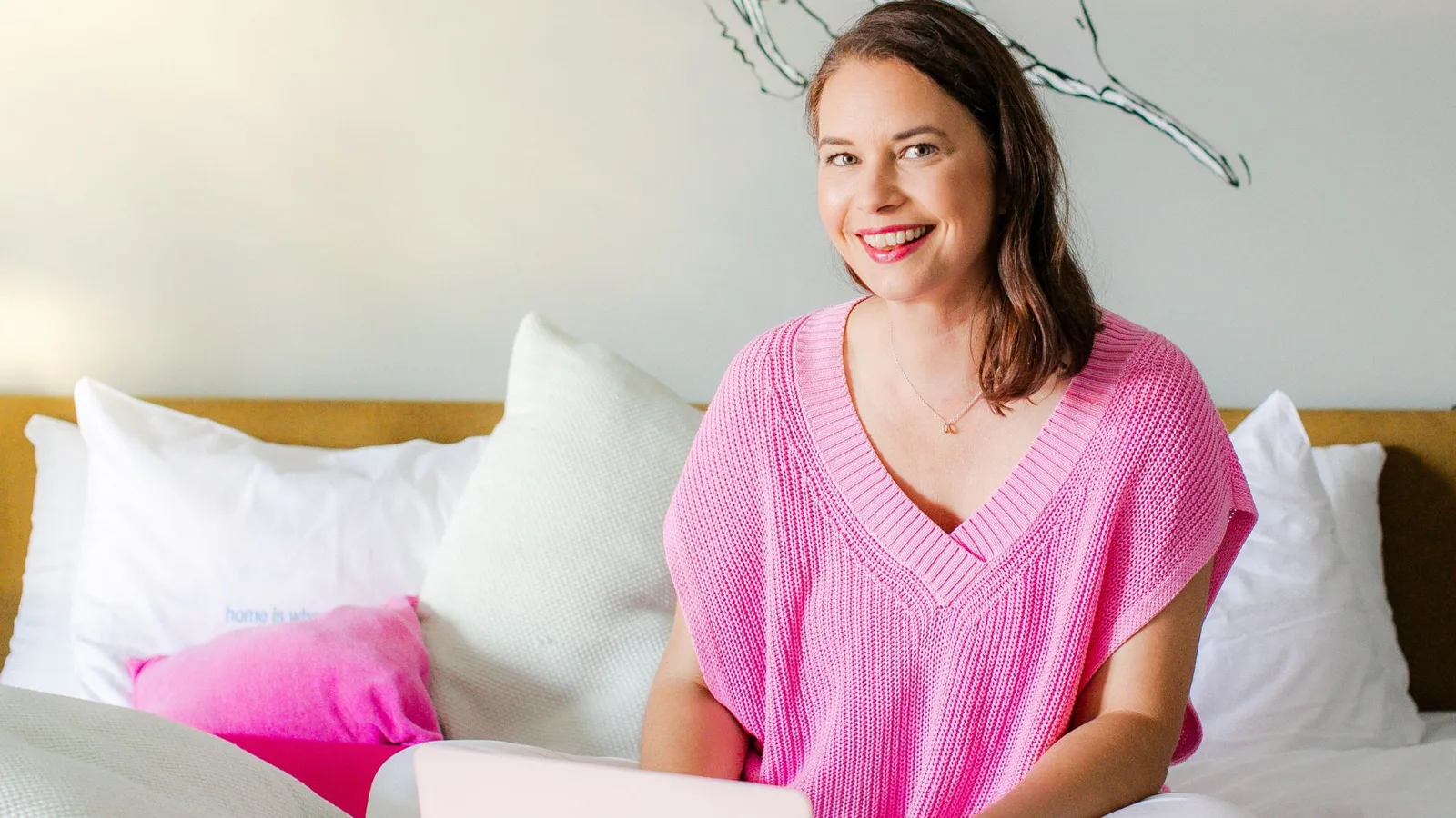 Simone Stalberg Großformat Portrait, Frau in rosa Pullover auf Bett mit Laptop