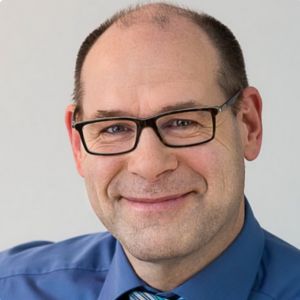 Jörg Küpper, Mann mit Brille im blauen Hemd vor grauem Hintergrund