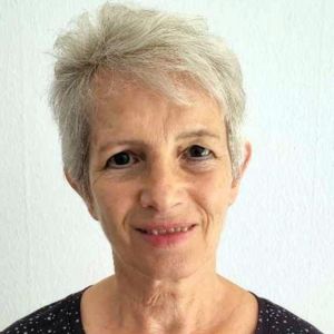 Noori Mitha, Frau mit grauem Haar und Lächeln vor grünem Hintergrund