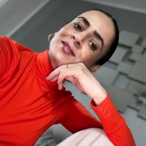 Fadma Hannane, Frau mit kurzem dunklem Haar im roten Shirt, Kopf auf Hand gestützt