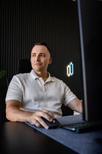 becomePro 3 Mann am Schreibtisch mit Computer, weißes Poloshirt, modernes Büro mit vertikalen Lamellen und Neonlicht