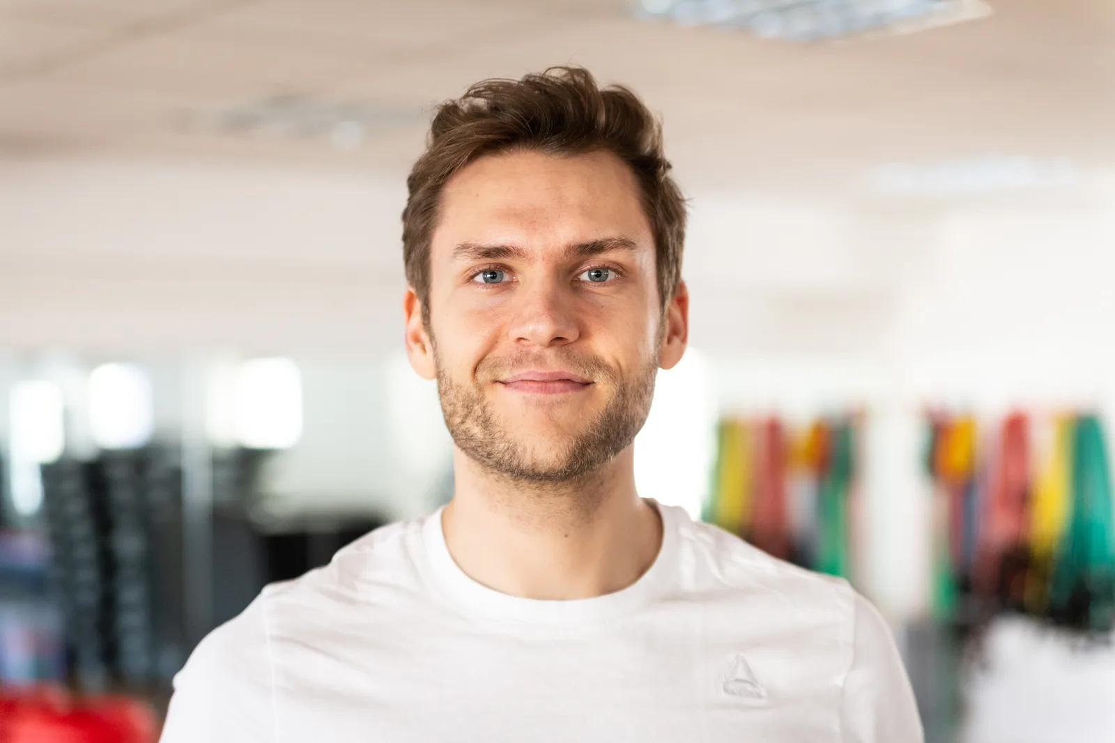Porträt von Movement Coach Mike, junger Mann mit braunen Haaren in weißem Shirt im Studio