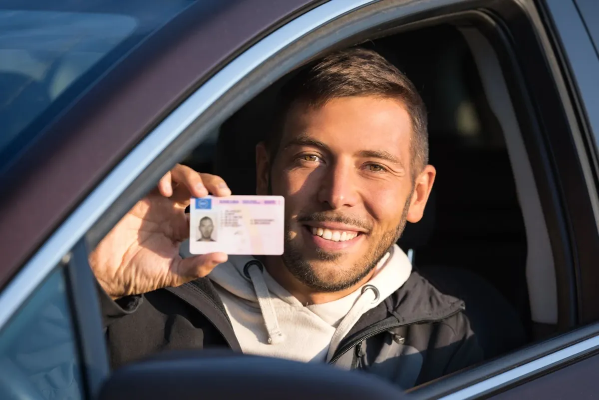 MPU-Vorbereitung online – mit Plan zurück zum Führerschein 2 Lächelnder Mann zeigt aus Autofenster seinen Führerschein