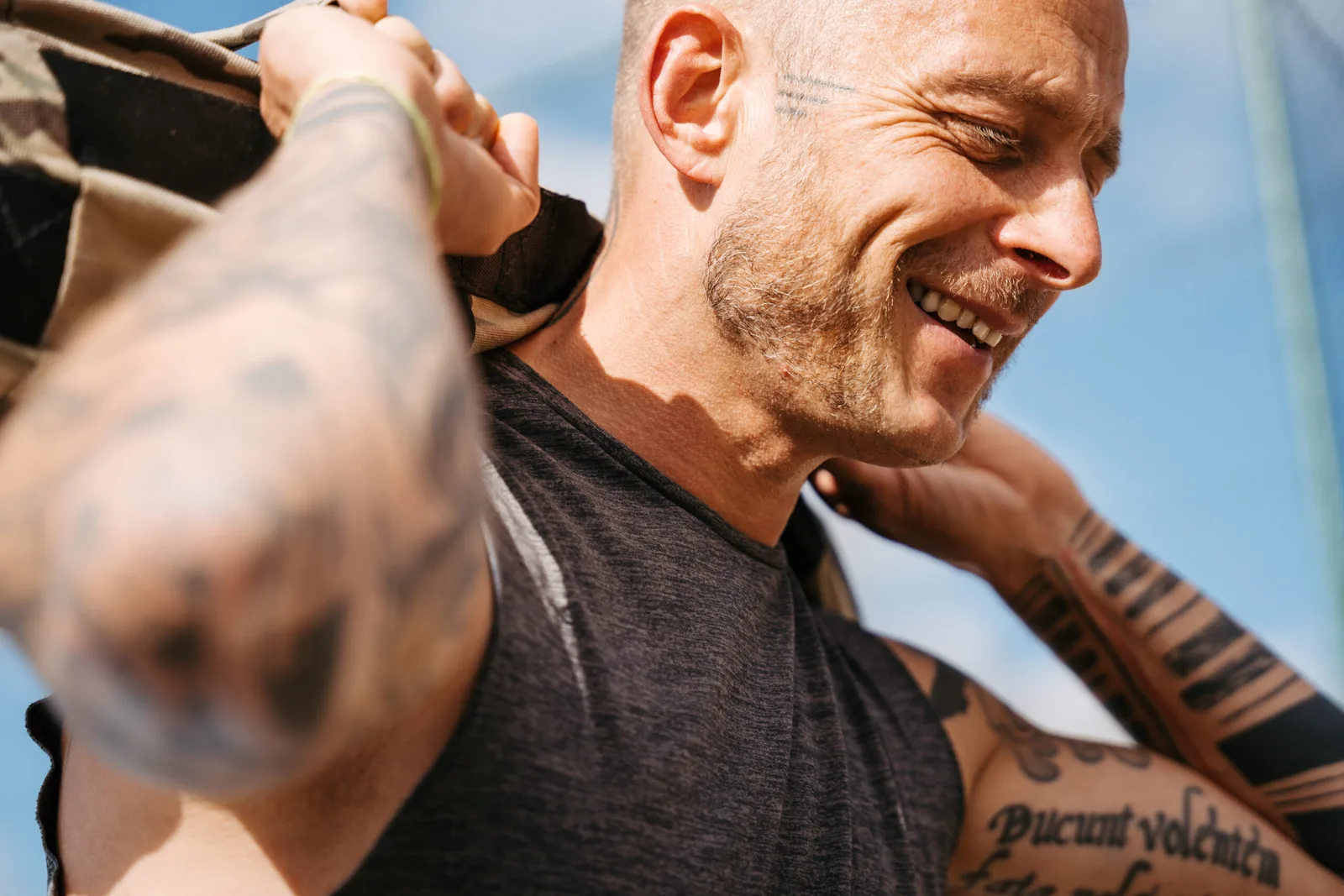 Nahaufnahme eines Mannes mit Tattoos beim Sandsacktraining, konzentrierter Gesichtsausdruck