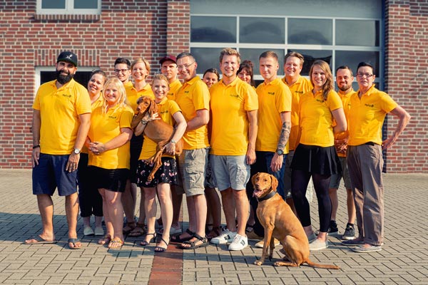 mydog365 Team in gelben Polo-Shirts mit Hunden vor Ziegelbau