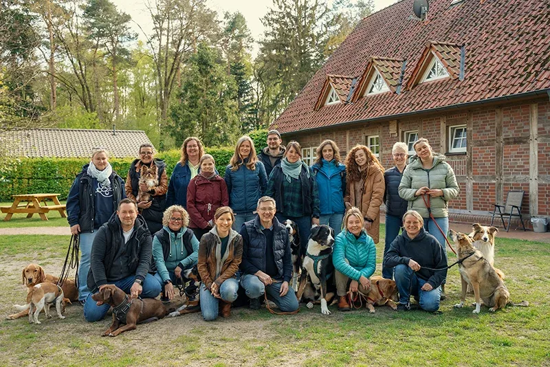 Gruppenfoto von Hundetrainern und Teilnehmern mit verschiedenen Hunden vor Backsteinhaus